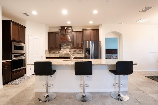 kitchen featuring visible vents, a sink, tasteful backsplash, appliances with stainless steel finishes, and custom exhaust hood
