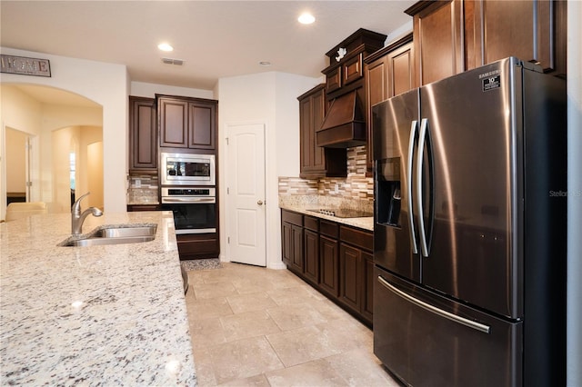 kitchen with a sink, stainless steel appliances, arched walkways, decorative backsplash, and custom exhaust hood