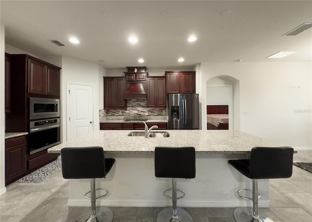 kitchen featuring tasteful backsplash, custom range hood, arched walkways, stainless steel appliances, and a sink