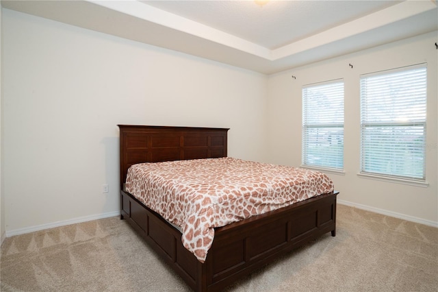 bedroom with a tray ceiling, baseboards, and light carpet