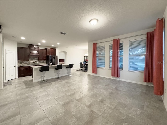 kitchen with a breakfast bar, stainless steel refrigerator with ice dispenser, backsplash, open floor plan, and arched walkways