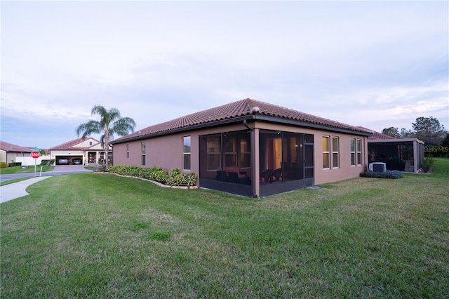 back of property featuring stucco siding, a tile roof, a yard, and a sunroom