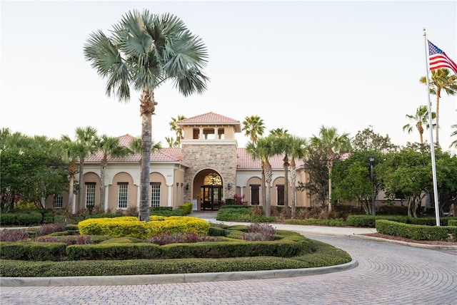 mediterranean / spanish home featuring a tile roof, stone siding, and stucco siding