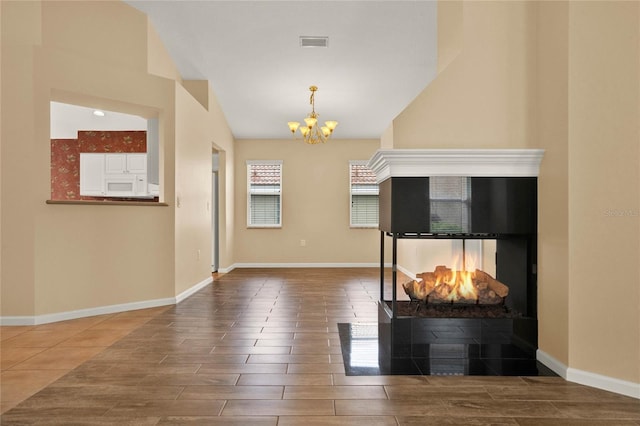 unfurnished living room featuring a fireplace, visible vents, baseboards, wood tiled floor, and an inviting chandelier