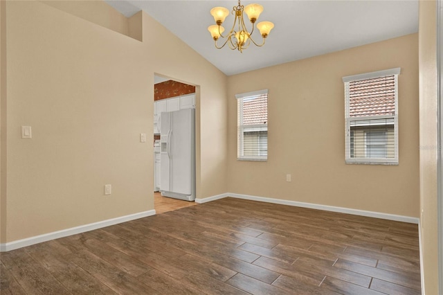 spare room featuring a chandelier, lofted ceiling, baseboards, and wood finished floors