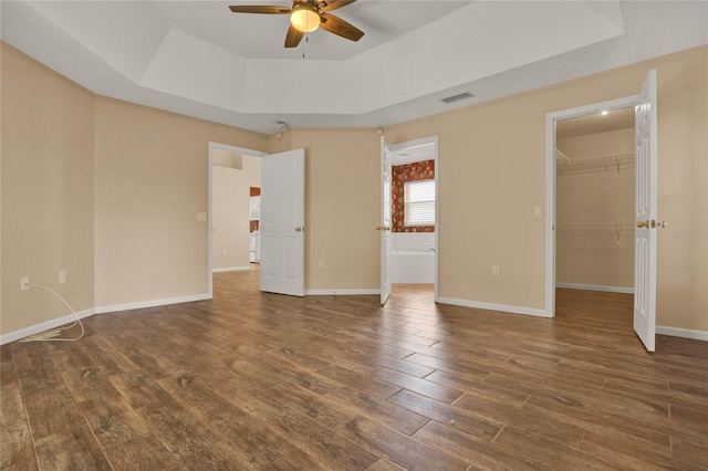 unfurnished bedroom featuring a walk in closet, a raised ceiling, visible vents, and wood finished floors