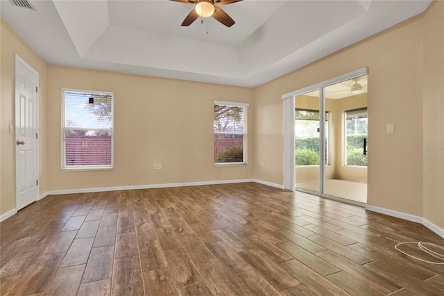 unfurnished room featuring ceiling fan, wood finished floors, visible vents, baseboards, and a raised ceiling