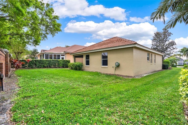 back of property featuring a yard, a tile roof, and stucco siding