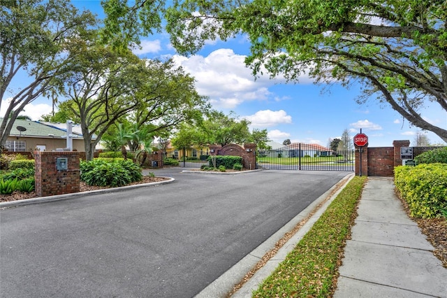 view of road with a gated entry, curbs, traffic signs, a gate, and sidewalks