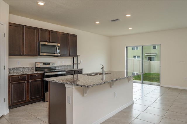 kitchen featuring stone counters, stainless steel appliances, visible vents, a sink, and an island with sink