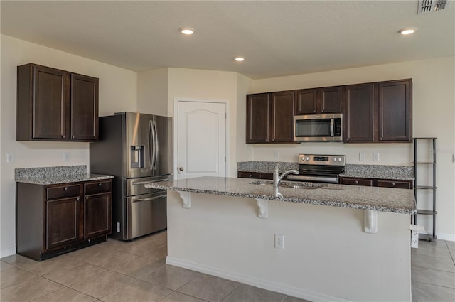 kitchen with stone countertops, appliances with stainless steel finishes, dark brown cabinets, and a breakfast bar area