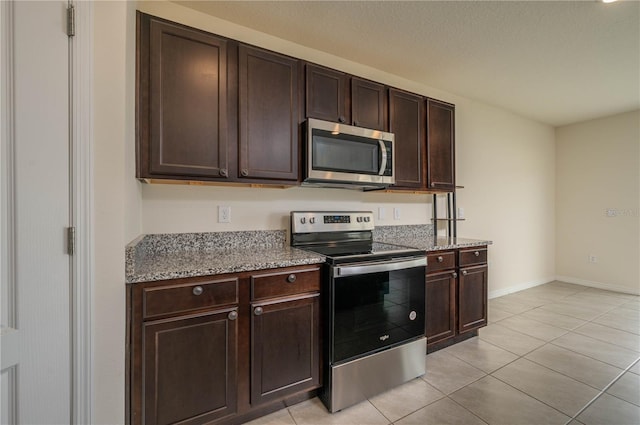 kitchen with light stone counters, light tile patterned floors, stainless steel appliances, dark brown cabinetry, and baseboards