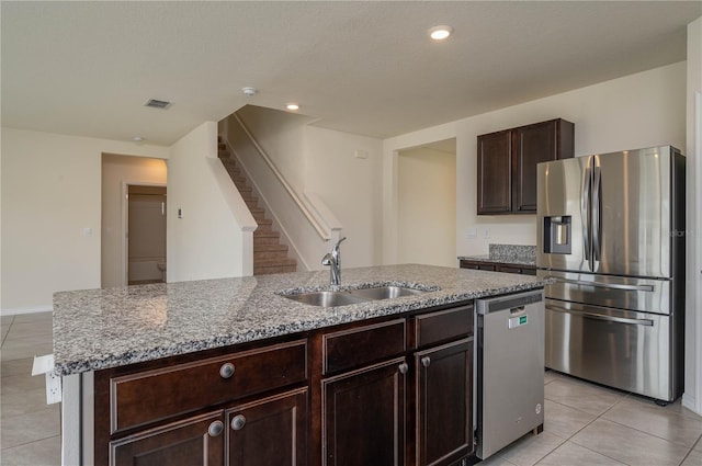 kitchen with light stone counters, a center island with sink, stainless steel appliances, visible vents, and a sink