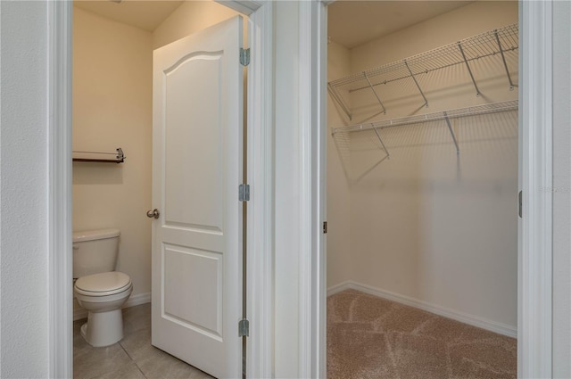 bathroom featuring toilet, baseboards, a walk in closet, and tile patterned floors