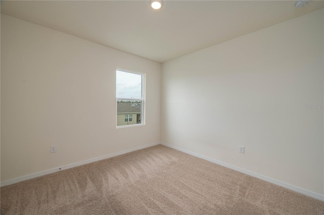 spare room featuring light carpet and baseboards