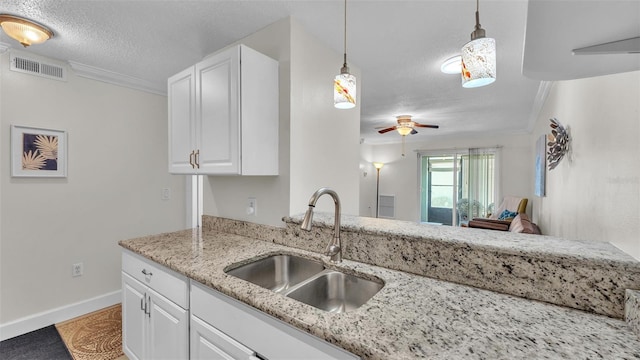 kitchen featuring a textured ceiling, a sink, visible vents, white cabinets, and light stone countertops