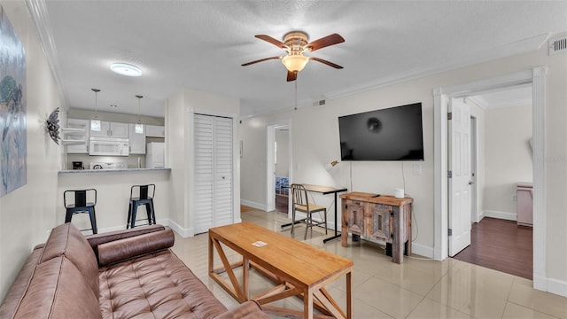 living room featuring light tile patterned floors, visible vents, a ceiling fan, a textured ceiling, and crown molding