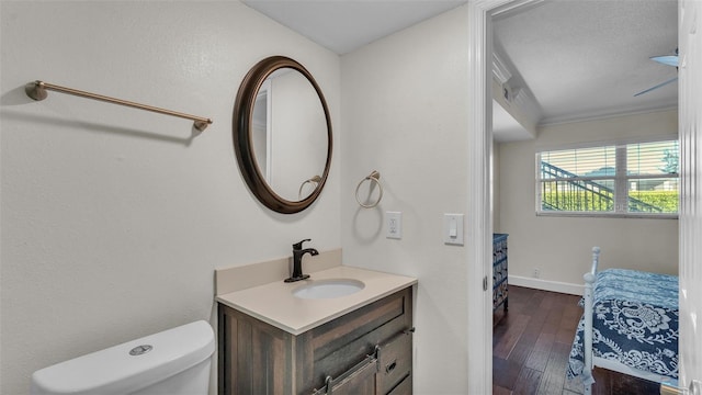 bathroom with toilet, ornamental molding, vanity, wood finished floors, and baseboards