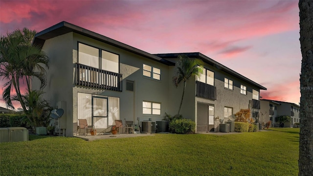 back of property with a patio area, cooling unit, a lawn, and stucco siding