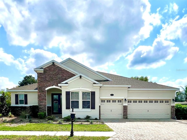 ranch-style home with an attached garage, a shingled roof, stucco siding, stone siding, and decorative driveway