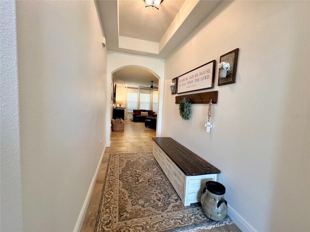 hall with arched walkways, stone finish floor, a raised ceiling, and baseboards