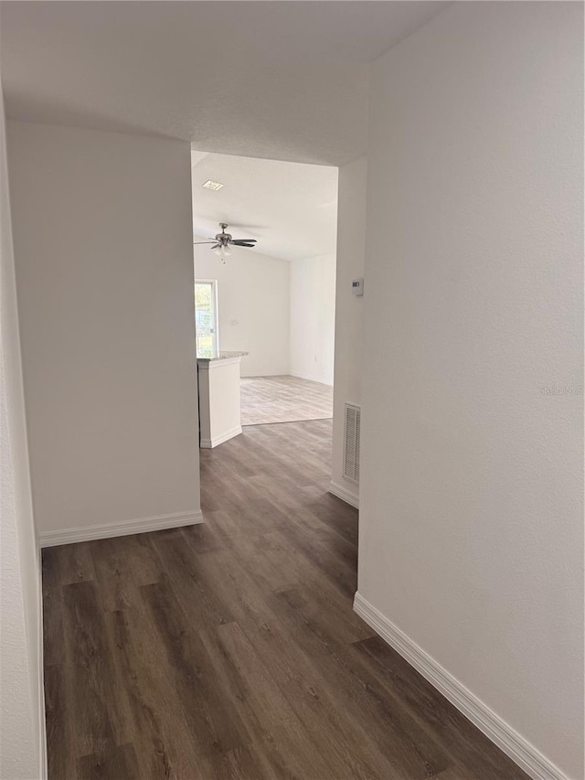 hallway with dark wood finished floors, visible vents, and baseboards