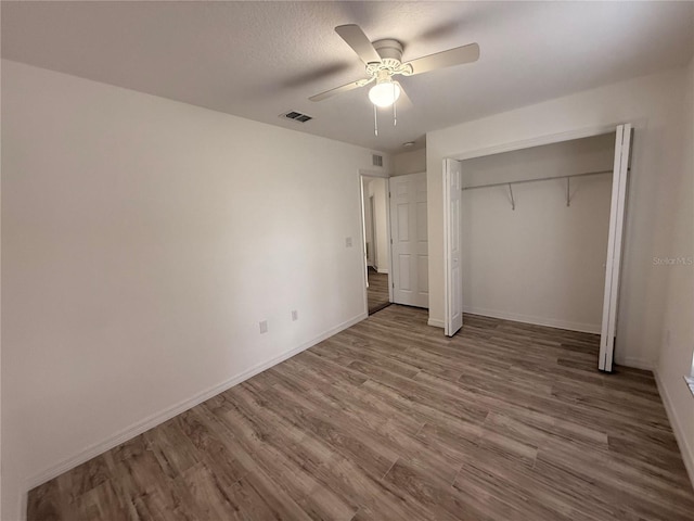 unfurnished bedroom with baseboards, visible vents, ceiling fan, wood finished floors, and a closet