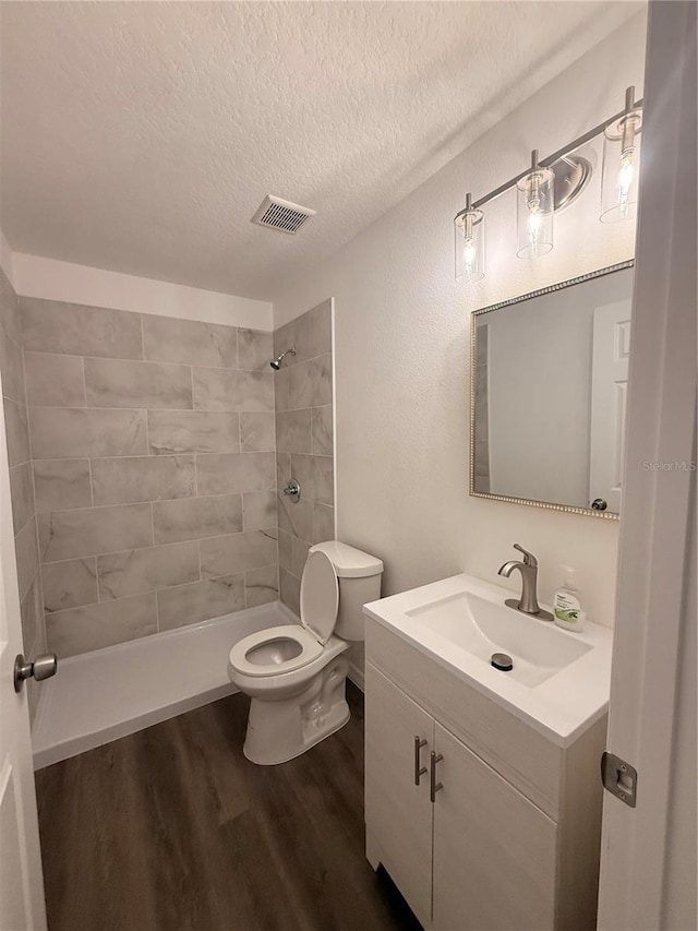 full bath featuring visible vents, toilet, vanity, wood finished floors, and tiled shower