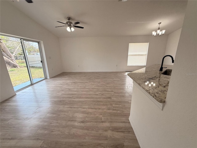 unfurnished living room featuring lofted ceiling, a sink, wood finished floors, baseboards, and ceiling fan with notable chandelier