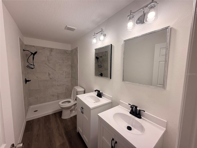 full bathroom with a tile shower, a textured ceiling, a sink, and visible vents