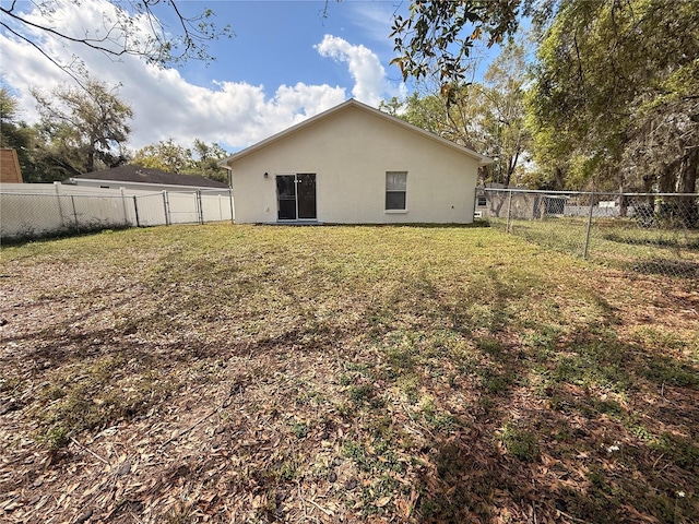 rear view of house featuring a yard, a fenced backyard, and stucco siding