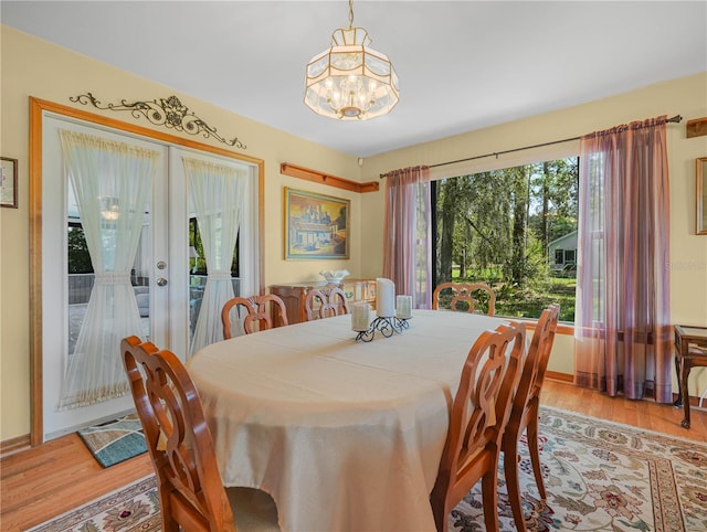 dining area with french doors, a notable chandelier, light wood-style flooring, and baseboards