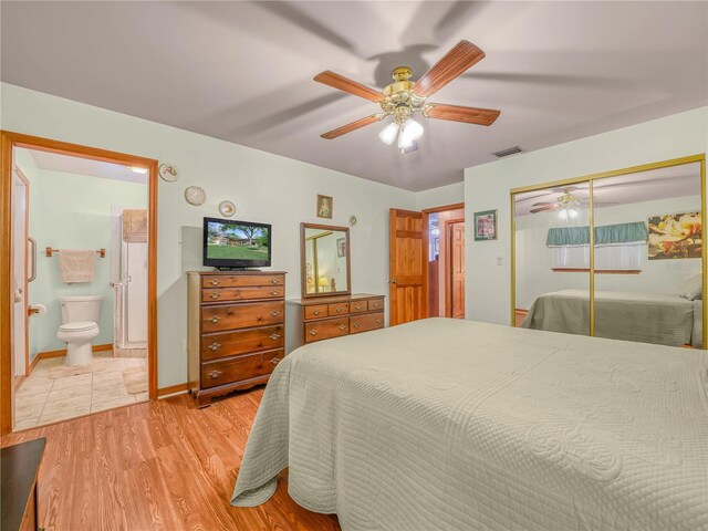 bedroom featuring a closet, visible vents, light wood-style flooring, ensuite bath, and baseboards