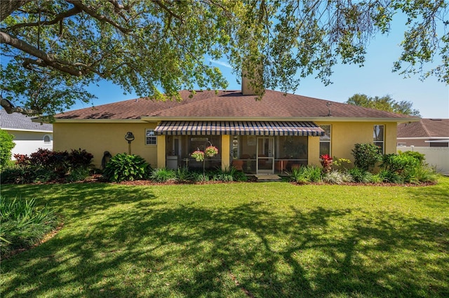 back of house featuring stucco siding, a lawn, fence, and a sunroom