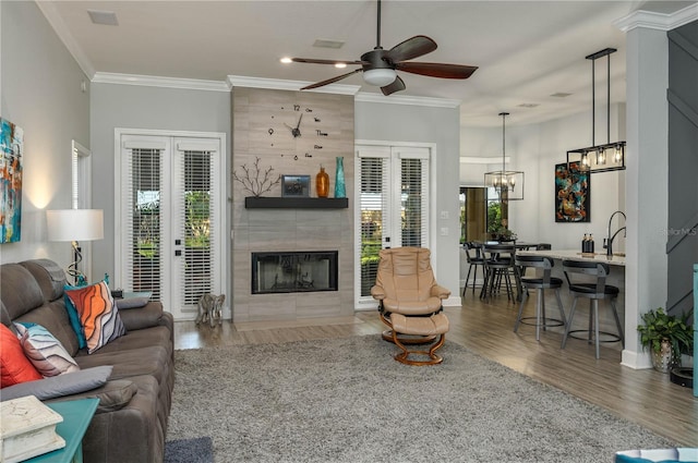 living room featuring ceiling fan with notable chandelier, wood finished floors, a fireplace, crown molding, and baseboards