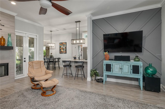 living room featuring crown molding, baseboards, a tiled fireplace, ceiling fan with notable chandelier, and wood finished floors