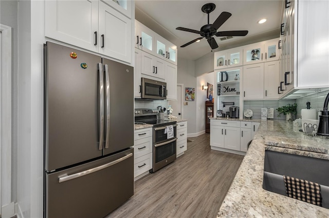 kitchen featuring light wood-style flooring, backsplash, white cabinetry, stainless steel appliances, and light stone countertops