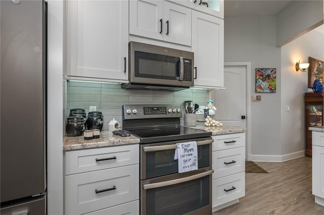 kitchen featuring baseboards, decorative backsplash, light wood-style floors, appliances with stainless steel finishes, and white cabinetry