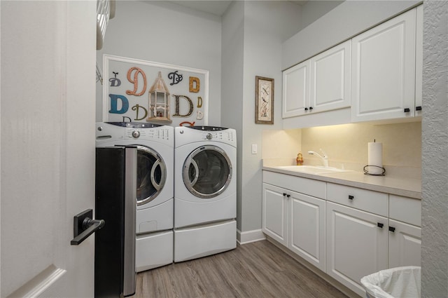 clothes washing area featuring washing machine and clothes dryer, cabinet space, light wood-style floors, and a sink