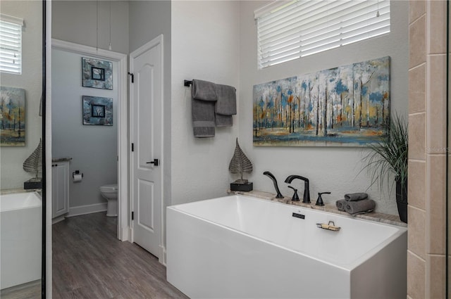 bathroom featuring wood finished floors, toilet, and a freestanding tub