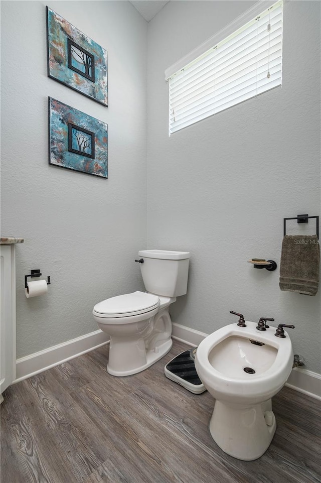 bathroom with toilet, a bidet, baseboards, and wood finished floors