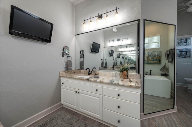 bathroom with vanity, wood finished floors, baseboards, toilet, and a textured wall