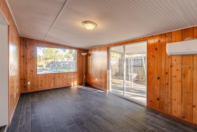 empty room featuring lofted ceiling, an AC wall unit, dark wood-style flooring, and a healthy amount of sunlight