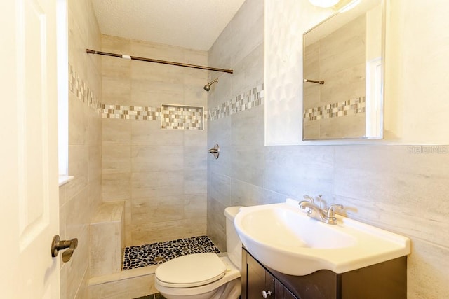 full bathroom featuring toilet, a tile shower, vanity, and tile walls