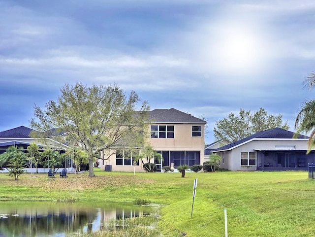 rear view of house with a lawn, a water view, a sunroom, and stucco siding