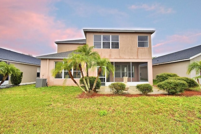 rear view of property featuring central AC, a lawn, a sunroom, and stucco siding