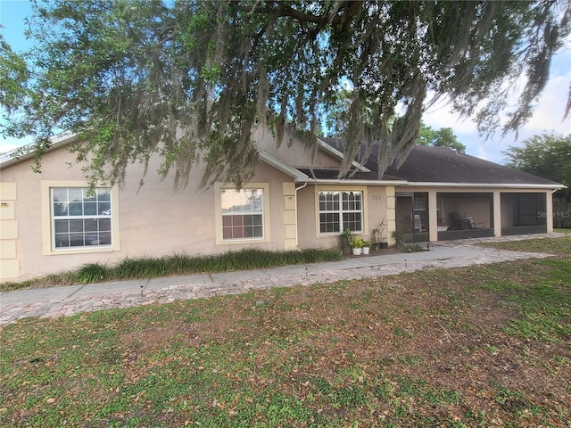 view of front of house with stucco siding, a front lawn, and a sunroom