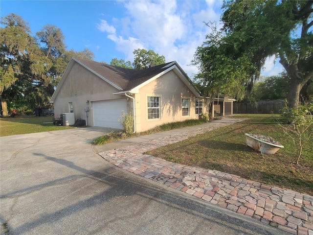 view of property exterior with driveway, an attached garage, central AC, stucco siding, and a lawn