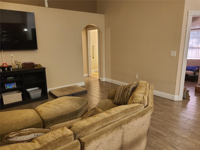 living room featuring arched walkways, baseboards, and wood finished floors