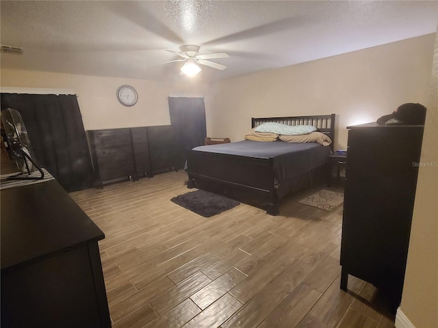 bedroom featuring visible vents, a textured ceiling, ceiling fan, and wood finished floors